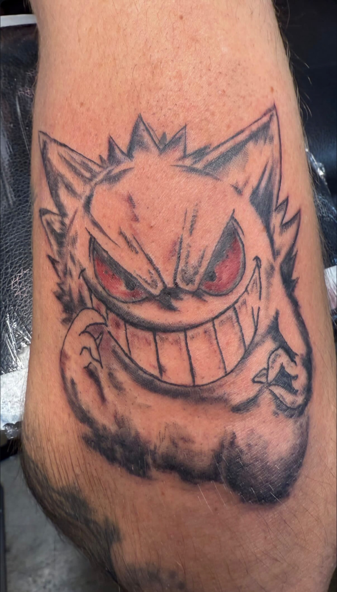 Gengar tattoo with red eyes and a wide grin on a forearm