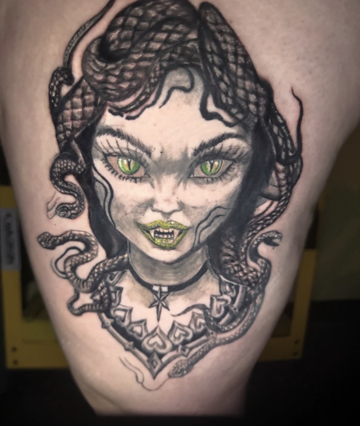 Black and grey Medusa portrait tattoo with green eyes, green lips and snake hair on a thigh